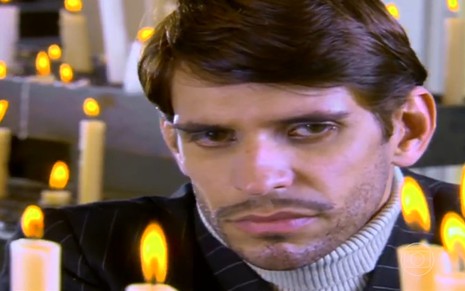 O ator Alexandre Barillari com expressão séria, em meio a velas, em cena de Alma Gêmea
