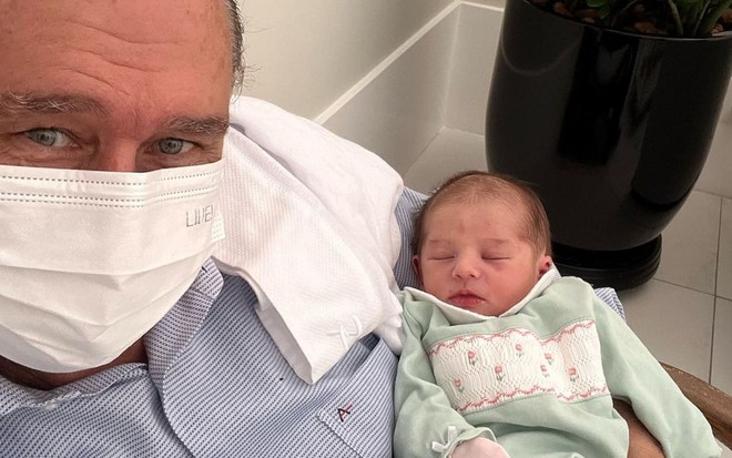 Álvaro José usa uma máscara branca e está com a neta, Pilar, apoiada no braço esquerdo