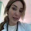 Amanda Meirelles usa um jaleco branco e está com os cabelos loiros presos num rabo de cavalo de lado; ela exprime cansaço em vídeo publicado nas redes sociais