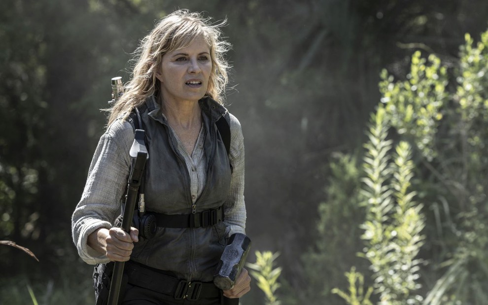 Kim Dickens tem expressão de choque em cena de Fear the Walking Dead; ela carrega uma bengala em uma mão e uma marreta na outra