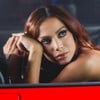 Anitta posa dentro de um carro vermelho, com a calça baixa deixando cofrinho à mostra