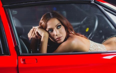 Anitta posa dentro de um carro vermelho, com a calça baixa deixando cofrinho à mostra