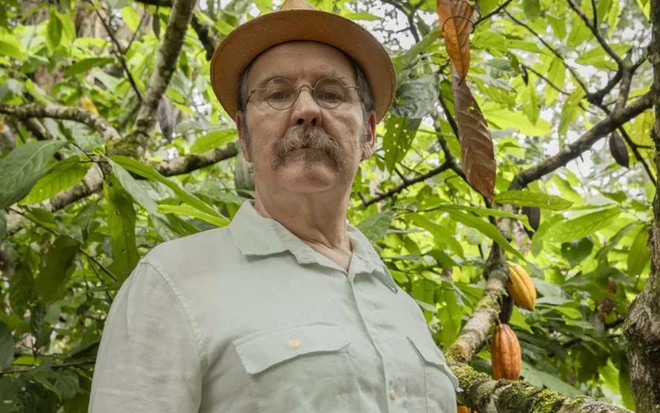 O ator Antonio Calloni caracterizado como coronel Belarmino, seu personagem em Renascer, com ecpressão séria, chapéu, em meio a árvores