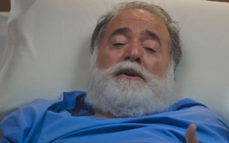Em cena de Terra e Paixão, Tony Ramos está na cama de um hospital com uniforme azul