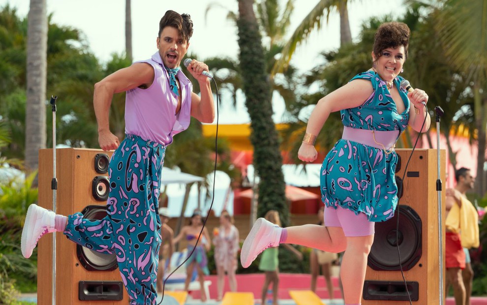 Com roupas chamativas, Rodrigo Urquidi e Rossana De Leon se apresentam em um palco à beira da piscina em cena de Acapulco