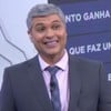 Joel Datena força sorriso no cenário do Brasil Urgente; a repórter Carine Roma está no telão do programa