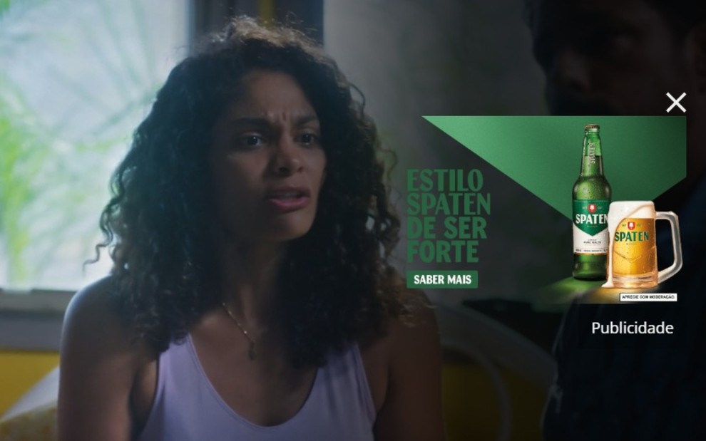 Bárbara Reis como Aline em cena da novela Terra e Paixão, em imagem escurecida e com publicidade à esquerda, no Globoplay