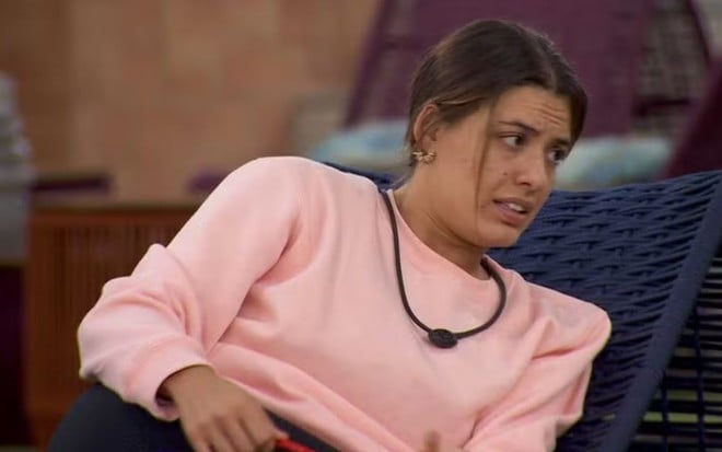 Beatriz Reis está deitada em um divã, na área externa do BBB 24, e conversa