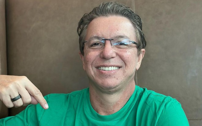 Boninho sorri e aponta para uma camiseta verde