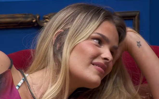 Yasmin Brunet está com deitada no sofá, com uma das mãos apoiadas na cabeça