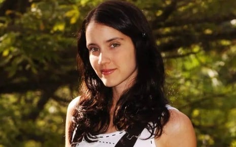 Patrícia Werneck caracterizada como Camila em Paraíso Tropical (2007), em paisagem externa com plantas, olhando séria para a câmera