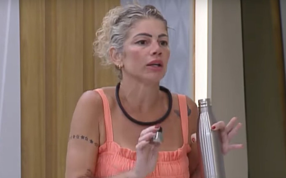 Catia Paganote gesticula e segura garrafinha na mão no quarto de A Grande Conquista 2