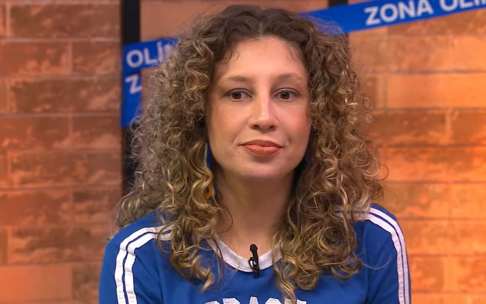 A influenciadora Nathaly Dias, com uma blusa azul escrita Brasil, com expressão séria no programa Zona Olímpica, da CazéTV