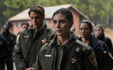 A brasileira Morena Baccarin tem expressão séria em cena de Fire Country; ela está vestida como xerife