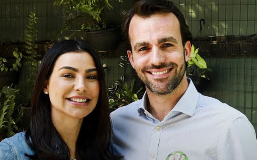 Cíntia Chagas e Lucas Bove estão abraçados e sorridentes, lado a lado
