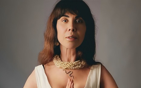 Claudia Alencar posa para foto com os cabelos soltos, um colar de pedras e está com a expressão séria