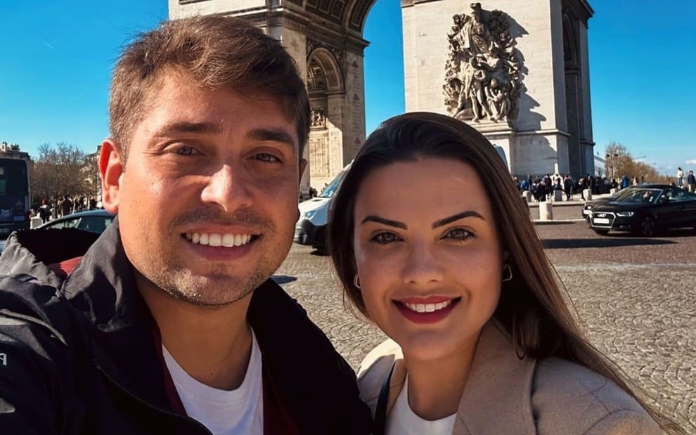 Danilo Santos Romano e a namorada, Thalita Valente, sorriem em frente ao Arco do Triunfo, em Paris, França