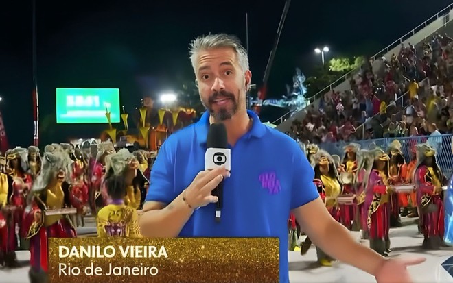Com blusa azul do uniforme Globeleza, Danilo Vieira está falando ao microfone na Marquês de Sapucaí