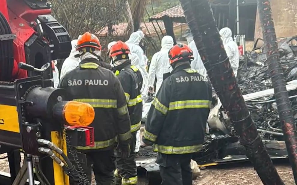 Bombeiros uniformizados estão ao redor dos escombros do avião