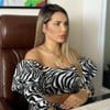 Deolane Bezerra está sentada com um cropped com estampa de zebra e analisa o monitor de um computador