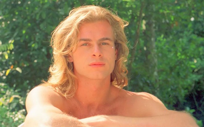 João Vitti caracterizado como Xampu na novela Despedida de Solteiro (1992), de cabelos loiros compridos, olhando para a câmera