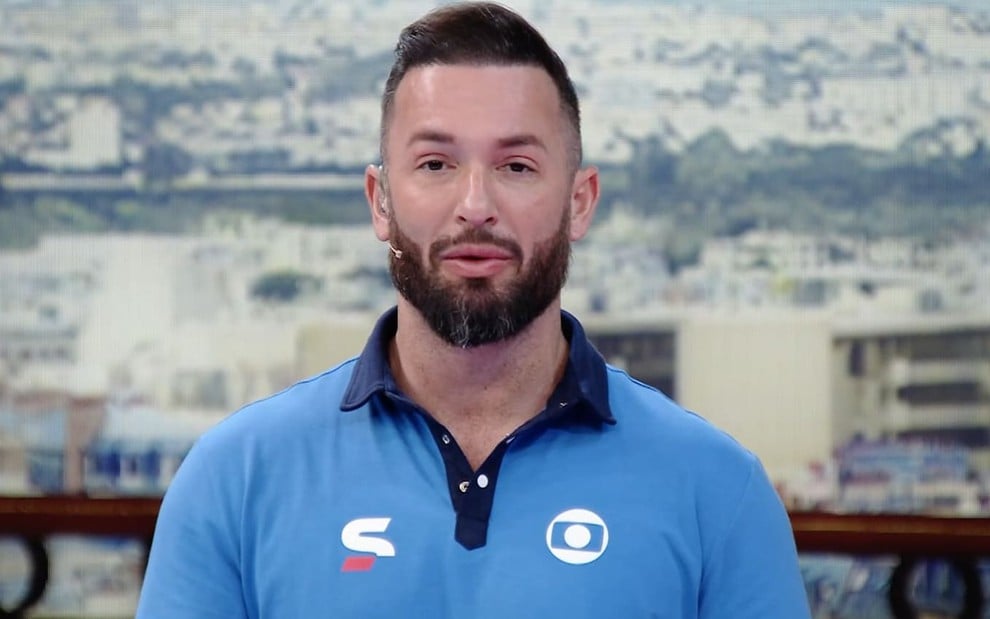 Diego Hypolito usa uma camiseta azul claro com o símbolo da Globo; ela está sério