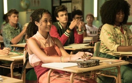 Jamilly Mariano está sentada em uma carteira de sala de aula, cercada de outros jovens
