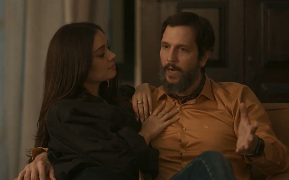 Em cena de Renascer, Sophie Charlotte e Vladimir Brichta estão abraçados, sentados no sofá