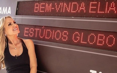 Eliana diante de uma claquete gigante em que se lê "Bem-vinda Eliana aos Estúdios Globo"