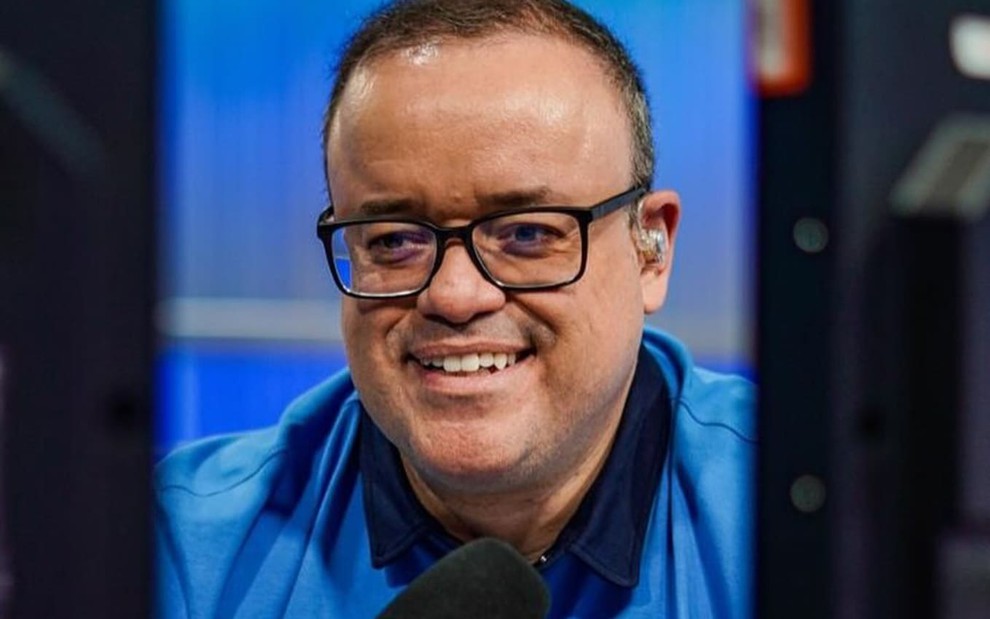 Everaldo Marques usa uma camisa polo azul e óculos de aros pretos; ele sorri