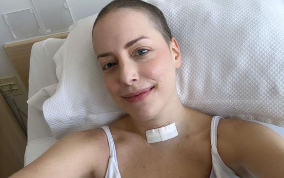 Fabiana Justus deitada em uma cama de hospital, com curativo no pescoço