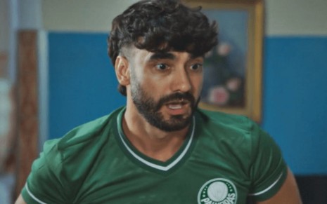 O ator Gabriel Godoy com expressão de susto, vestindo camisa do Palmeiras, em cena de Família É Tudo