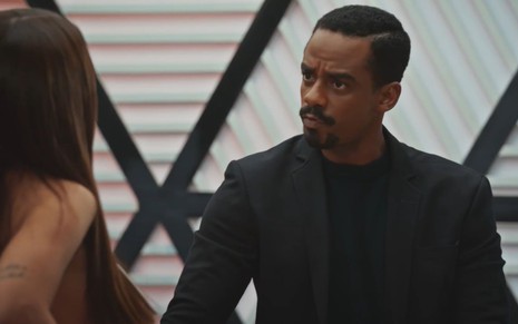 O ator Raphael Logam com expressão séria em frente à atriz Rafa Kalimann em cena da novela Família É Tudo