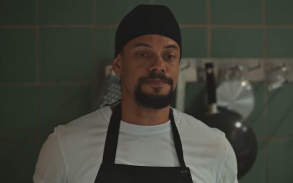 O ator Paulo Lessa com expressão séria, uniforme de cozinheiro, em cena de Família É Tudo