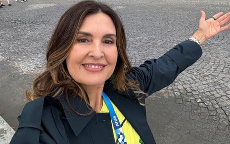 Fátima Bernardes usa um blazer e uma camisa do Brasil; ela está sorridente e estende os braços em uma praça em Paris, na França