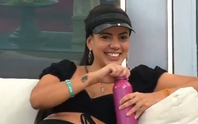 Foto de Fernanda Bande no BBB 24; ela veste top preto, boné preto e segura garrafa rosa