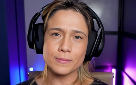 A jornalista Fernanda Gentil com um headphone preto, grande, olha diretamente para a câmera em um close no rosto