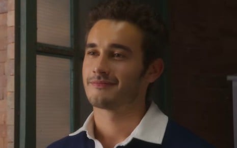O ator Filipe Bragança com expressão feliz, leve sorriso de boca fechada, em cena de Elas por Elas