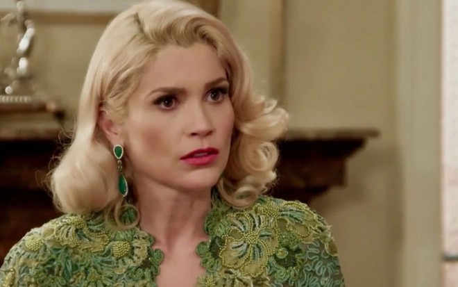 Flávia Alessandra caracterizada como Sandra; ela usa o cabelo curto e loiro e exprime choque em cena de Êta Mundo Bom!