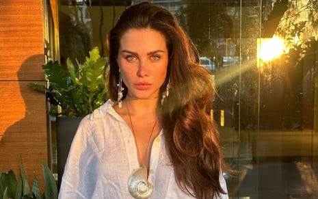 Flavia Pavanelli com uma blusa branca e um colar dourado toma sol