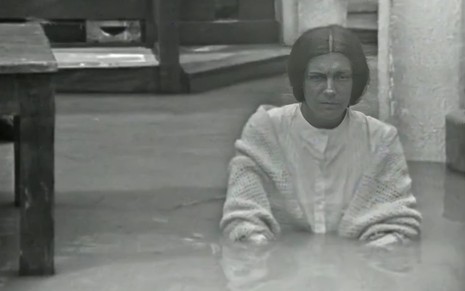 A atriz Neuza Amaral em meio a sala inundada, com água pela cintura, em cena da novela Fogo Sobre Terra (1974)