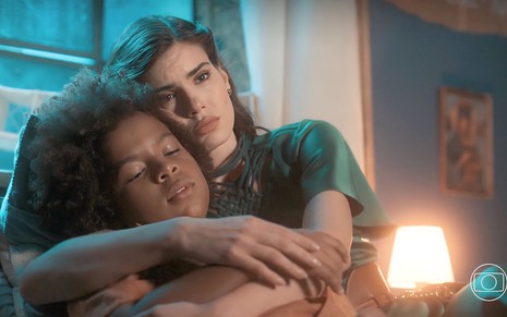 Camila Queiroz está em uma cama abraçada com o ator mirim Levi Aasf em cena da novela Amor Perfeito
