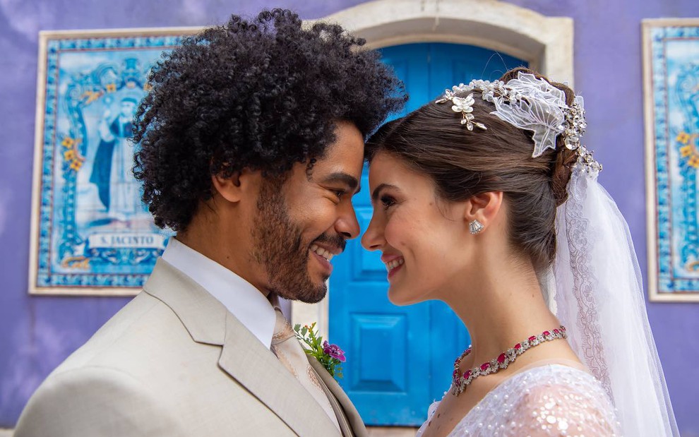 Diogo Almeida está encarando Camila Queiroz com o rosto colado ao dela em cena de casamento da novela Amor Perfeito