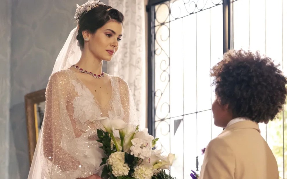 Camila Queiroz caracterizada como Marê; ela está com os cabelos amarrados em um coque e usa um vestido de noiva. O semblante exprime alegria em cena de Amor Perfeito.