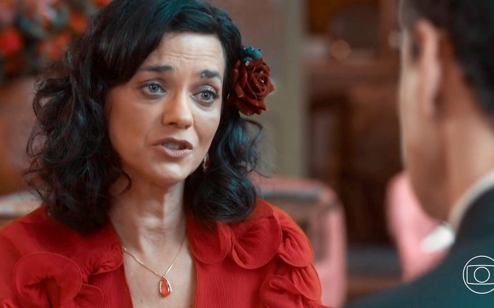 Ana Cecília Costa conversa com Carmo Dalla Vecchia, cortado na imagem, em cena de Amor Perfeito em que us traje vermelho