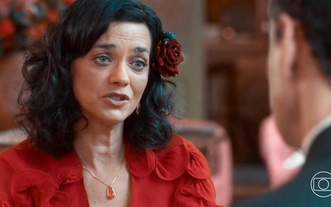 Ana Cecília Costa conversa com Carmo Dalla Vecchia, cortado na imagem, em cena de Amor Perfeito em que us traje vermelho