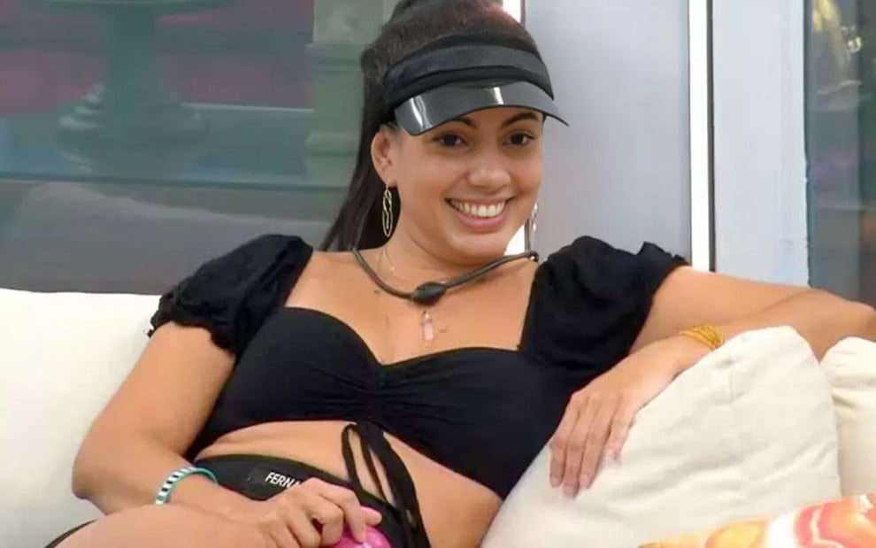 Fernanda Bande com uma viseira sentado no sofá da área externa do BBB 24