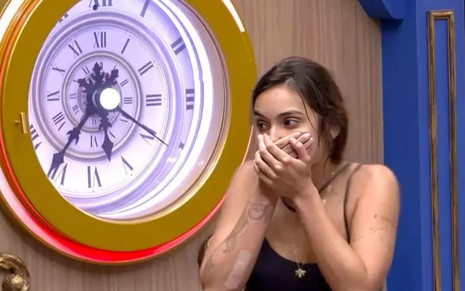 Vanessa Lopes leva a mão à boca em expressão de surpresa ao lado de um relógio com números romanos no BBB 24