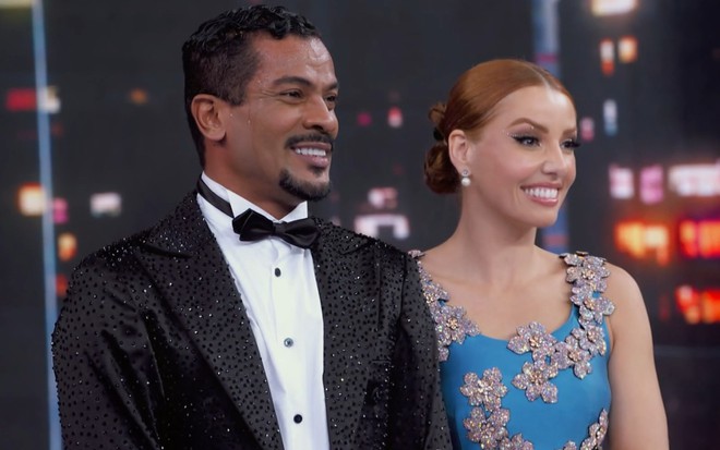 Samuel de Assis sorri enquanto transpira com smoking no palco da Dança dos Famosos; ele está ao lado da professora Larissa Parison