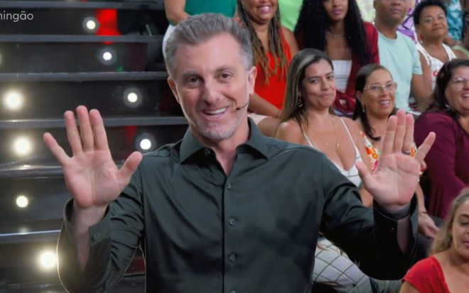 Luciano Huck com as mãos para cima no auditório do Domingão